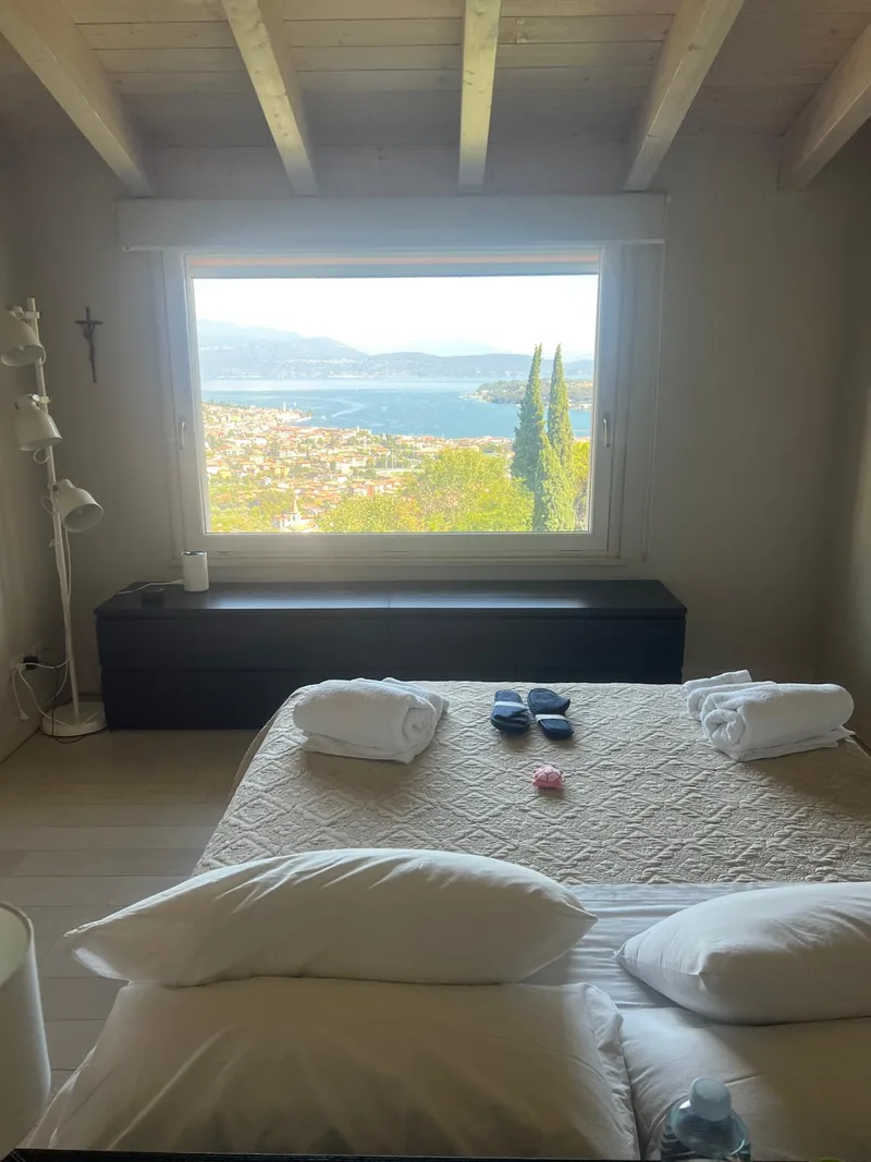 Tweepersoonsbed met handdoeken, lichte balken en een raam met uitzicht op het meer